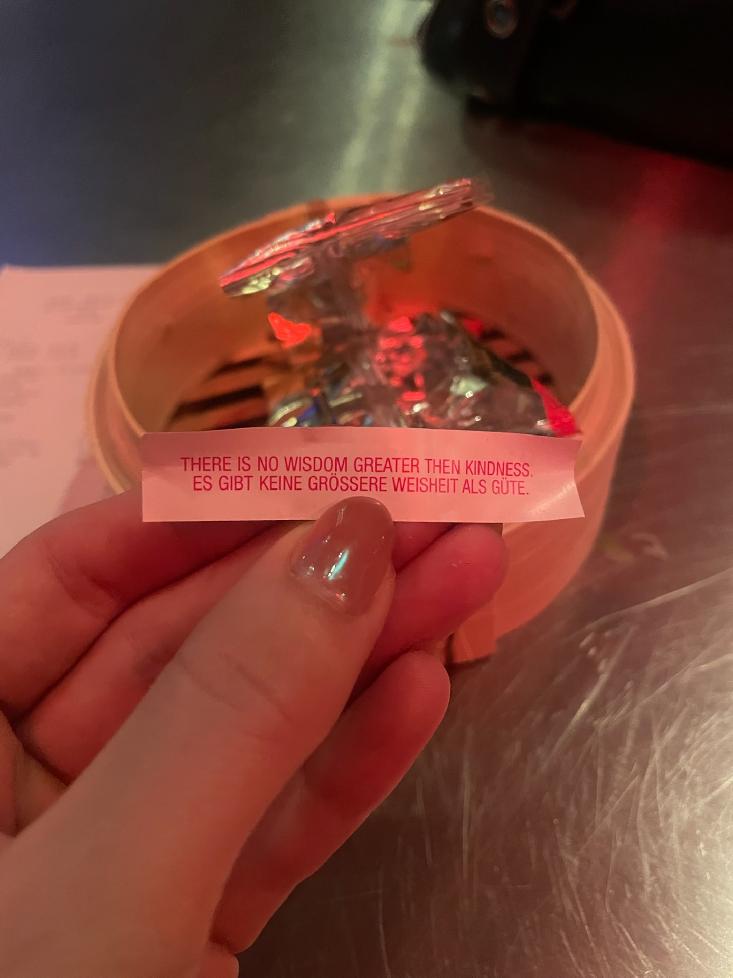 A hand holding a fortune cookie slip over a bamboo steamer in a dimly lit restaurant