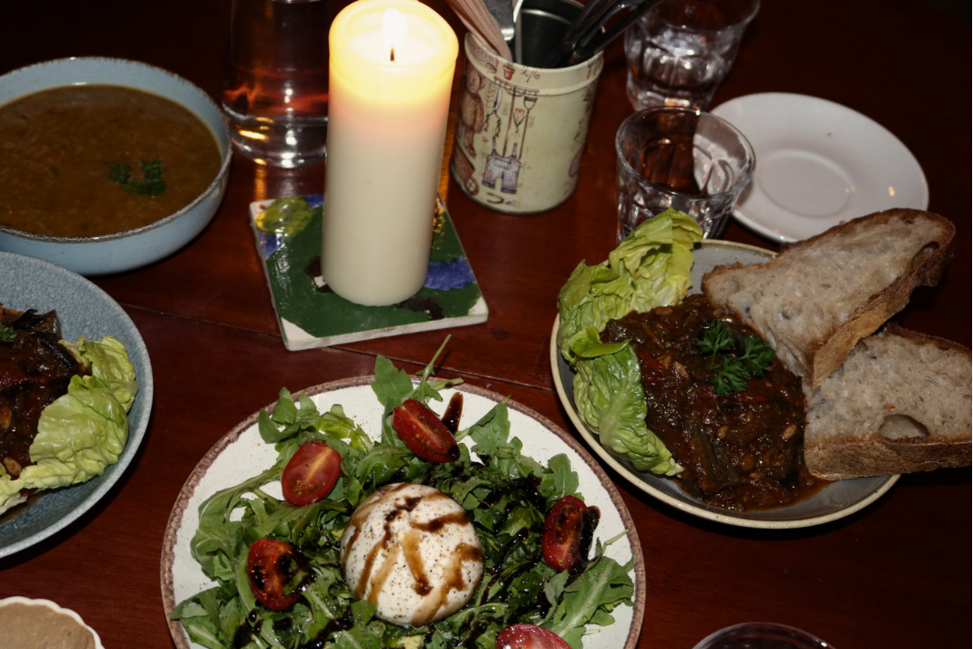 Candlelit dinner spread with burrata salad, stews and bread on a wooden table